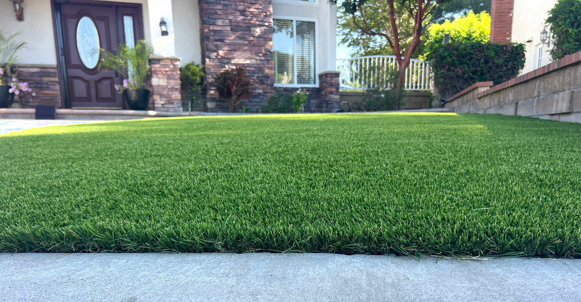 Front-yard artificial turf lawn installed flush with the driveway, blades standing tall and upright